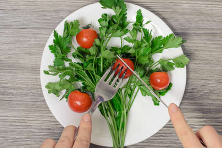 Close up top view photo of woman's hands cut cherry tomato on plate with parsley in form of green treeの写真素材