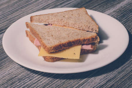 Delicious cheese sausage sandwich on a white round plate. Wooden background, horizontal view, vintage effectの写真素材