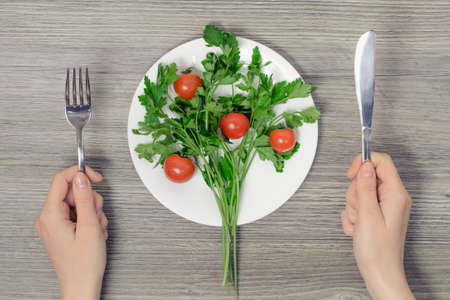 Concept of vegetarianism. Tio view  photo of wonam's hands and plate with cherry tomatoes and parsley on wooden tableの写真素材