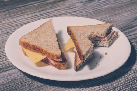 Close up of tasty bitten cheese sandwich on a round plate. Wooden background, horizontal viewの写真素材