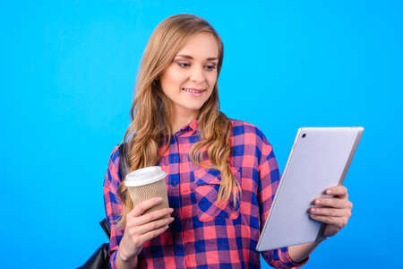 Close up portrait of attractive confident cheerful excited smart clever glad businesswoman freelancer enjoying tea shop watching video on pda pad in hand isolated on blue backgroundの写真素材