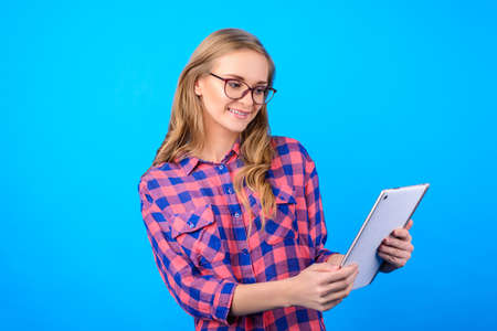 Side profile half-turned portrait of cheerful lovely sweet cute charming beautiful kind with long blonde hair manager agent checking information news on pad isolated on blue backgroundの写真素材