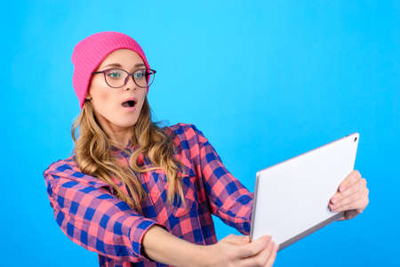 Modern technology concept. Close up portrait of frightened terrified scared shocked beautiful crazy cute woman playing computer games on digital gadget tablet isolated on blue background copy-spaceの写真素材