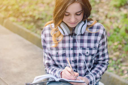 Young beautiful inspired girl in checkered shirt with headphones writing in her notebookの写真素材