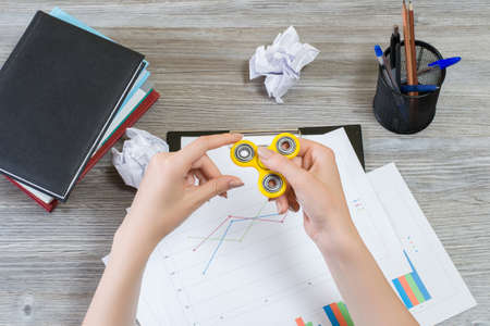 Top view photo of woman's hands playing with fidget spinner while having break at work. Popular and...