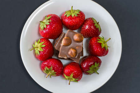 Plate full of tasty juicy strawberries and chocolate isolated on black background