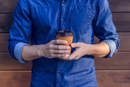 Man in jeans shirt holding cup of fresh coffee against brown backgroundの写真素材