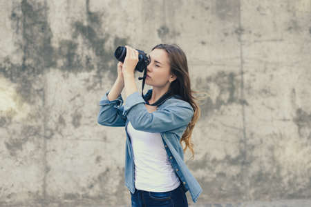 Woman is taking photo against grey background. She is dressed in jeans shirt and she has long hair.の写真素材
