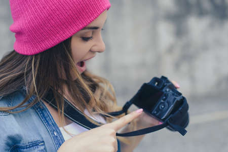 Smiling woman in casual clothes and pink hat holding camera and showing good shot she made during...