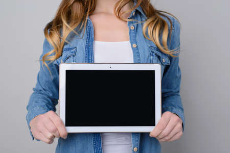 Woman in jeans shirt holding digital table with blank black screen for text. he is isolated on grey...
