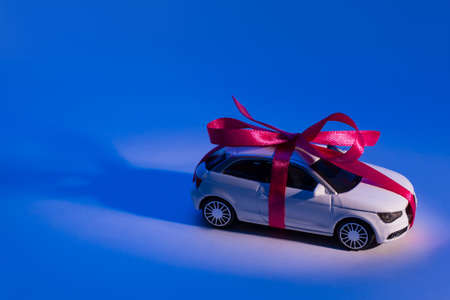 Close up profile side view photo of beautiful toy small modern trendy fashionable stylish car with pink ribbon and bow in spotlight searchlight isolated on blue backgroundの写真素材
