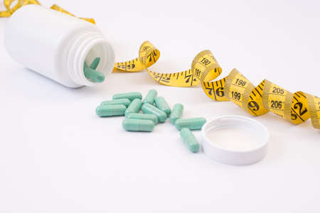 Obese pharmaceutical reduction vitamins medication gym lid cap screw concept. Close up photo of split full green capsules on table with yellow tape measure isolated on white background copy-spaceの写真素材