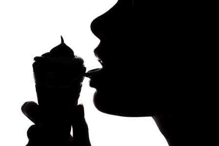 Side half-faced portrait of young woman's silhouette licking tasty ice-creamの写真素材