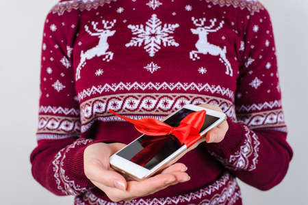Perfect surprise for new year! Cropped close up photo of modern stylish trendy smart phone in woman's hands with bow isolated on grey backgroundの写真素材