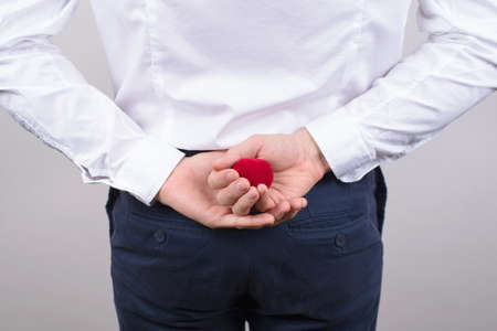 Bedind rear view photo of excited nervous gentleman hiding small bright red box with ring behind...