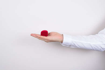 Side profile closeup cropped photo of hand holding closed red heart shaped small little box with...