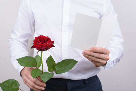 Cropped close up photo of cheerful handsome smiling sincere falling in love guy opening his heart to beloved lady reading poem holding card post card in hands isolated grey backgroundの写真素材
