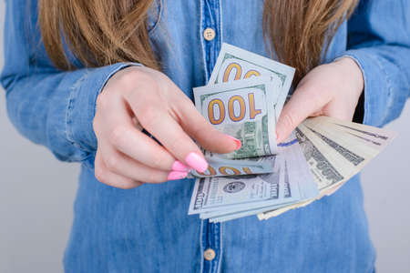 Cropped close-up photo of girlish beautiful hands with long nails pink bright manicure on fingers holding calculating old money wearing denim clothes isolated grey backgroundの写真素材