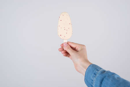 Close up pov first person cropped view photo of hand in denim clothes holding tasty yummy ice cream cover in white chocolate isolated grey background copyspaceの写真素材