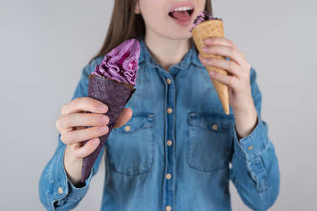 closeup photo portrait of pretty girl holding two nice looking tasty delicious chocolate ice creams in hands biting one isolated grey backgroundの写真素材
