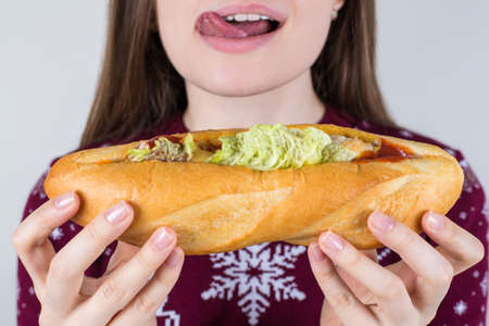 Unhealthy eating concept. Cropped closeup photo of cheerful excited nice crazy tongue-out fast food eater holding huge sandwich in hands isolated grey backgroundの写真素材