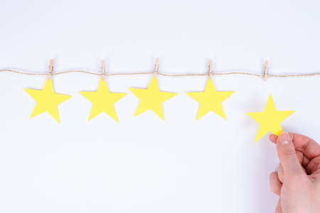 Young woman is giving her feedback by placing fifth star to the rating holding small star isolated white backgroundの写真素材