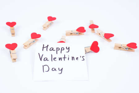 Happy Saint Valentines Day concept. Close-up photo of paper sticker with congratulation on it and lot of clothespins in shape of heart isolated white backgroundの写真素材