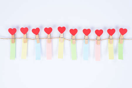 Photo of small clothespins in shape of hearts hanging on rope with small vertical colorful reminders...