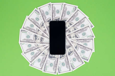 Top above close up view photo of black telephone on heap pile of bucks with empty touchscreen for text isolated green bright color backgroundの写真素材