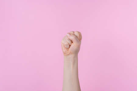 Strength concept. Cropped close up photo of fist raised in air isolated pink backgroundの写真素材