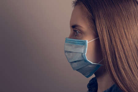 Novel coronavirus spreading concept. Closeup photo portrait of confident infected woman wearing medical facial mask looking aside isolated grey dark background empty spaceの写真素材