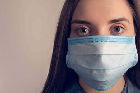 Cropped close up photo of upset girl wearing medical blue mask looking at camera isolated over grey background with copy spaceの写真素材