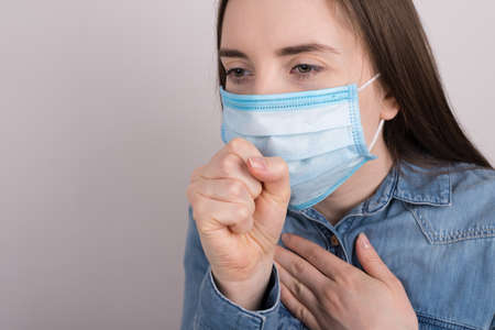 Cropped close up side profile view photo of sad upset unhappy woman in jeans shirt coughing holding hand fist near mouth face isolated grey background with copy empty spaceの写真素材