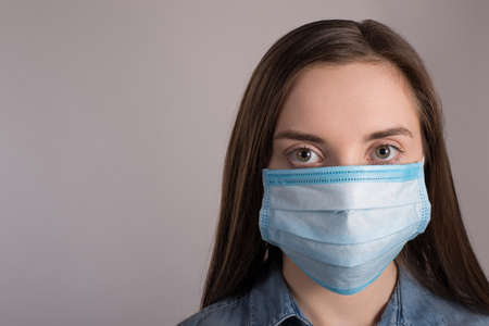 Coronavirus outbreak concept. Close up photo of woman wearing facial medical mask protecting against pandemic isolated over grey background with copy empty spaceの写真素材
