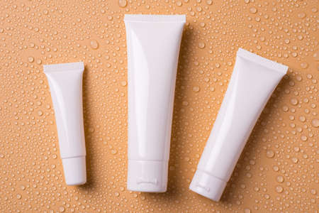 Top above overhead view photo of different size containers for blank empty cleanser toner tonic conditioner isolated over water drops beige backgroundの写真素材