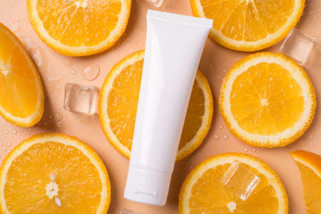 Bodycare concept. Top above flat lay close up view photo of tube with cream with no label empty copy blank space lying on beige background made of orange slicesの写真素材