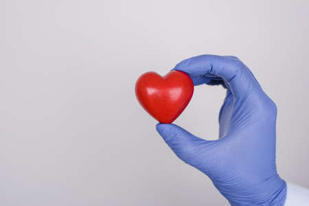 Cropped close up photo of hand in nitrile latex glove holding showing little red heart isolated over...
