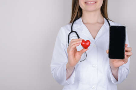 Communication on distance helping remote concultation concept. Cropped close up photo of hand holding showing touchscreen on device and small red heart isolated over grey backgroundの写真素材