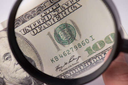 Fake money concept. Cropped close up photo of human finding false cash looking through magnifying glassの写真素材