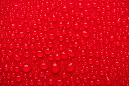 Close up cropped view photo image of shiny burgundy maroon bright color waterdrops on red backgroundの写真素材