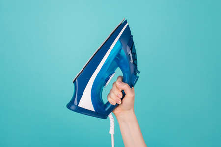 Housekeeping concept. Cropped photo of woman holding an electrical iron isolated on teal color...