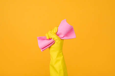 Cropped close-up photo of a hand in yellow glove holding a pink rubber for dusting isolated on yellow background. Housekeeping conceptの写真素材