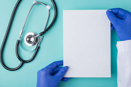 Top above overhead view photo of doctor holding a sheet of paper with a stethoscope isolated on turquoise backgroundの写真素材