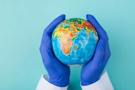Top above overhead close up view photo of a globe in doctor's hands isolated on turquoise backgroundの写真素材