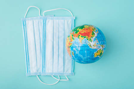 Top above overhead view photo of masks and an Earth globe isolated on turquoise background. Worldwide health protection during Coronavirus outbreak conceptの写真素材