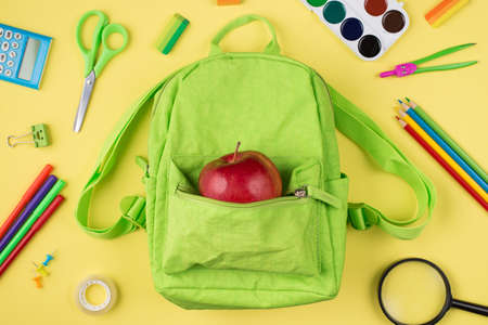 Top above overhead view photo of apple green backpack colorful stationery isolated on yellow backgroundの写真素材