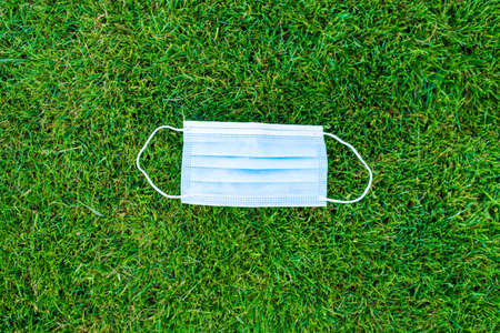Top above overhead close up view photo of used disposable medical blue mask lie on green grass