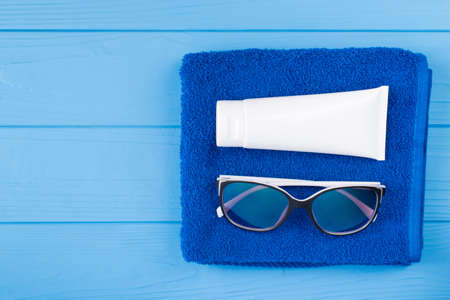 Sunbathing concept. Top above overhead view close-up photo of towel sunglasses and sunscreen isolated on blue wooden background with copyspaceの写真素材