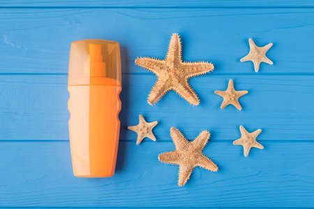 Top above overhead view close-up photo of sunscreen and starfish isolated on blue wooden background...