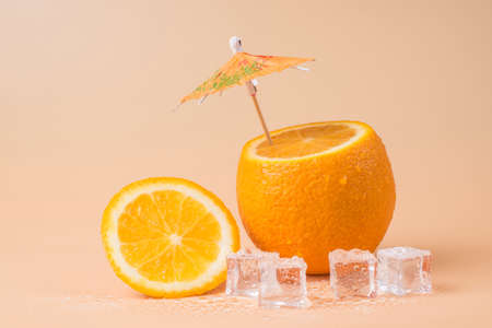 Close-up photo of cut orange with a cocktail umbrella in it and ice cubes isolated on sandy backgroundの写真素材